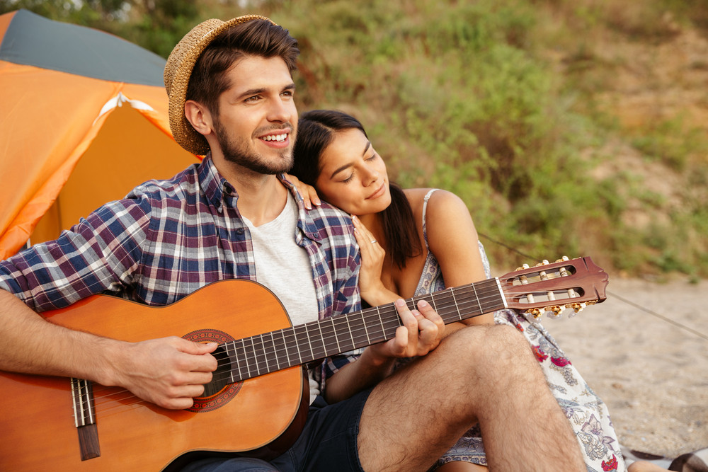 Young beautiful happy couple playing guitar while sitting at the beach