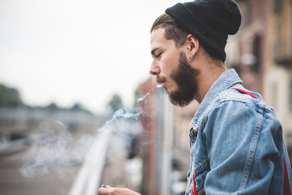 young handsome bearded hipster man smoking cigarette in the city ...