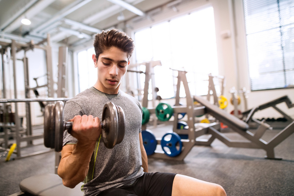 Young hispanic fitness man in gym sitting on bench, working out with ...