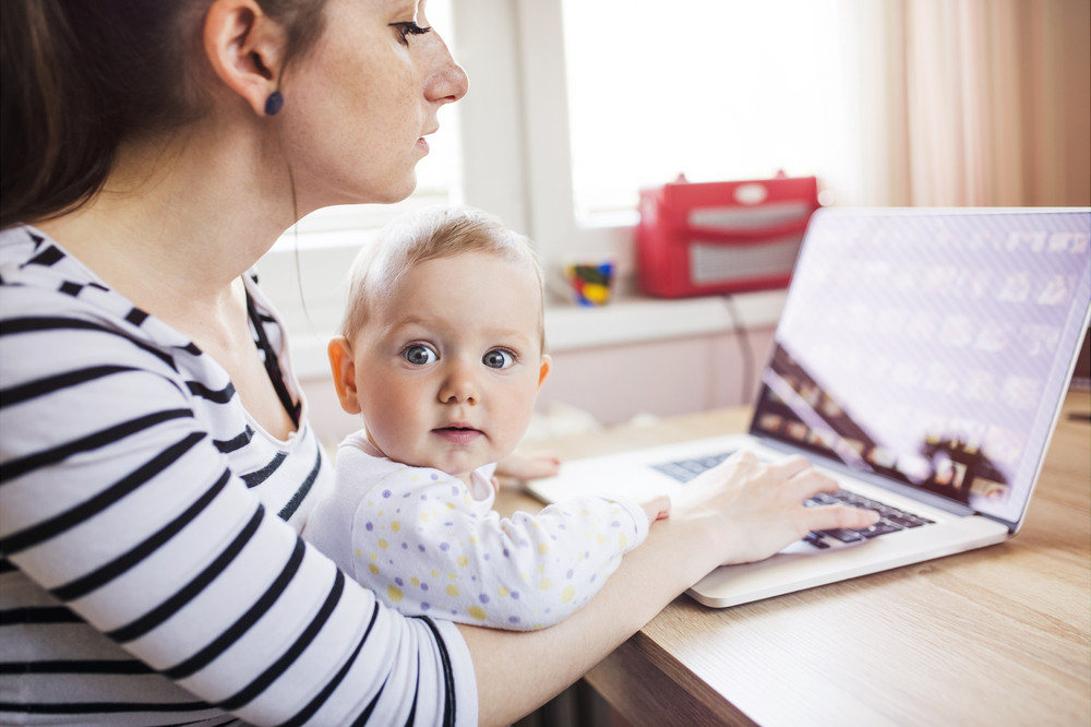 Young mother in home office with computer and her daughter
