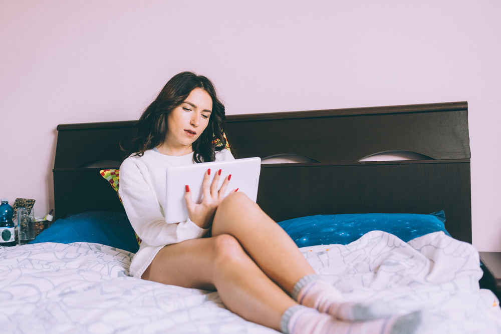 Young Woman Using Tablet Lying On Bed At Home Relaxing In