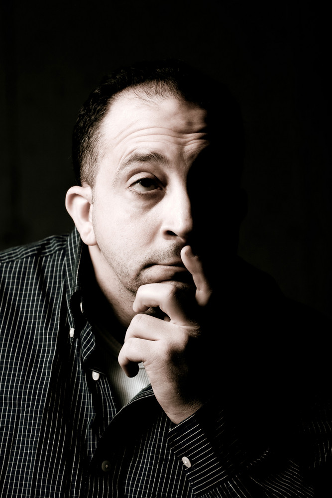 High contrast portrait of a middle aged man with a contemplative look on his face. He could be worried or anxious about something on his mind.