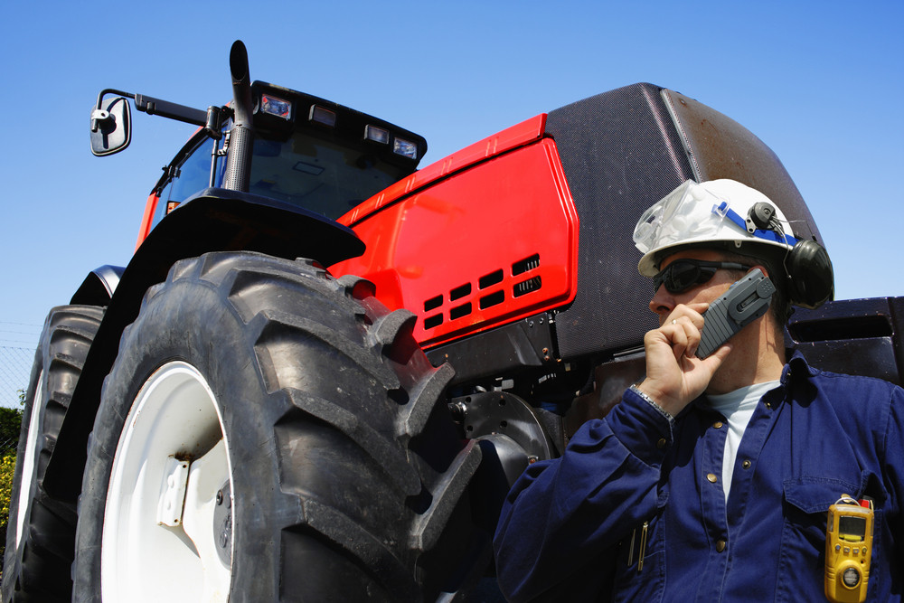 mechanic talking in phone, large tractor in background