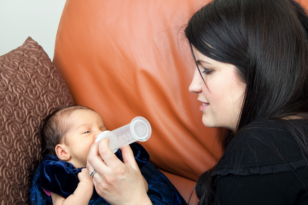 Mother feeds her newborn infant feeds on a bottle of baby formula.