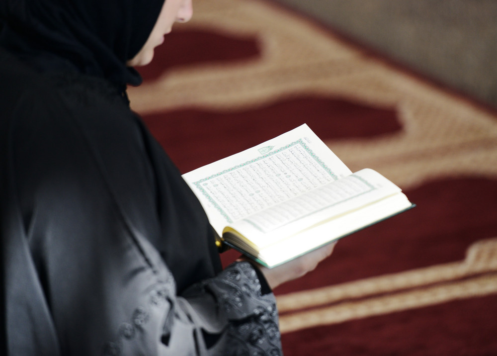 Muslim Arabic woman sitting and reading holy book Koran