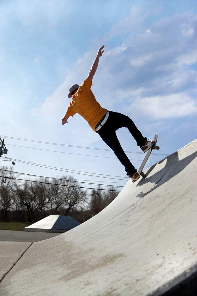 Portrait of a young skateboarder skating down a ramp at the skate park ...