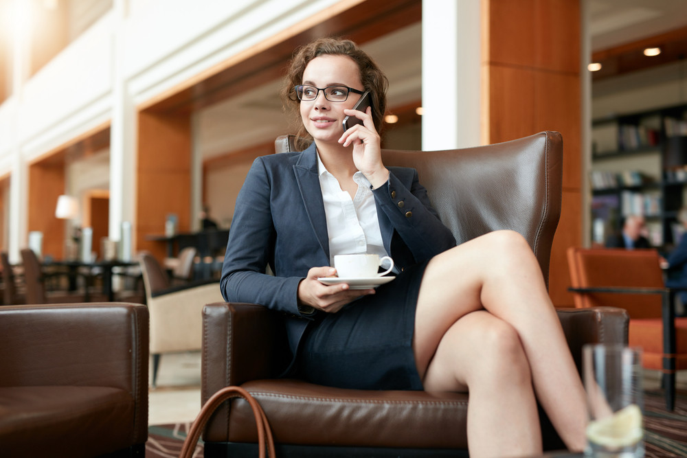 Portrait of happy young businesswoman sitting in cafe talking on mobile phone. Female executive with cup of coffee using cell phone and looking away.