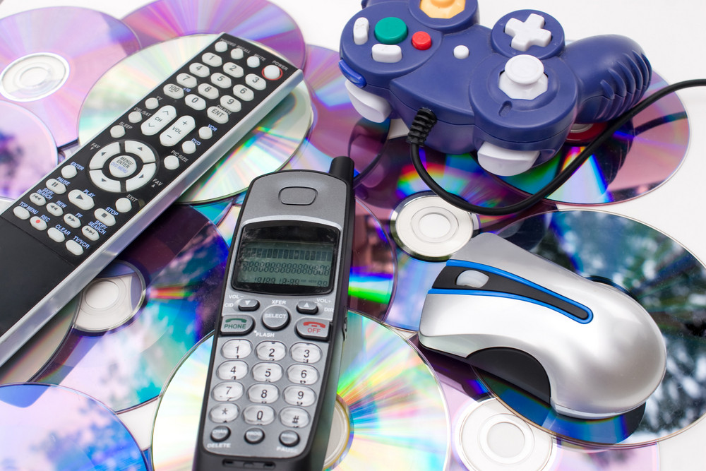 Remote control wireless computer mouse cordless telephone and video game controller over a bed of dvd disks isolated over white.