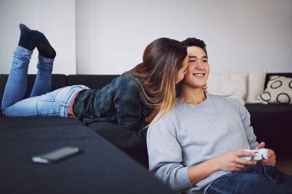 Teenage couple in living room. Beautiful woman cares her boyfriend playing video game.