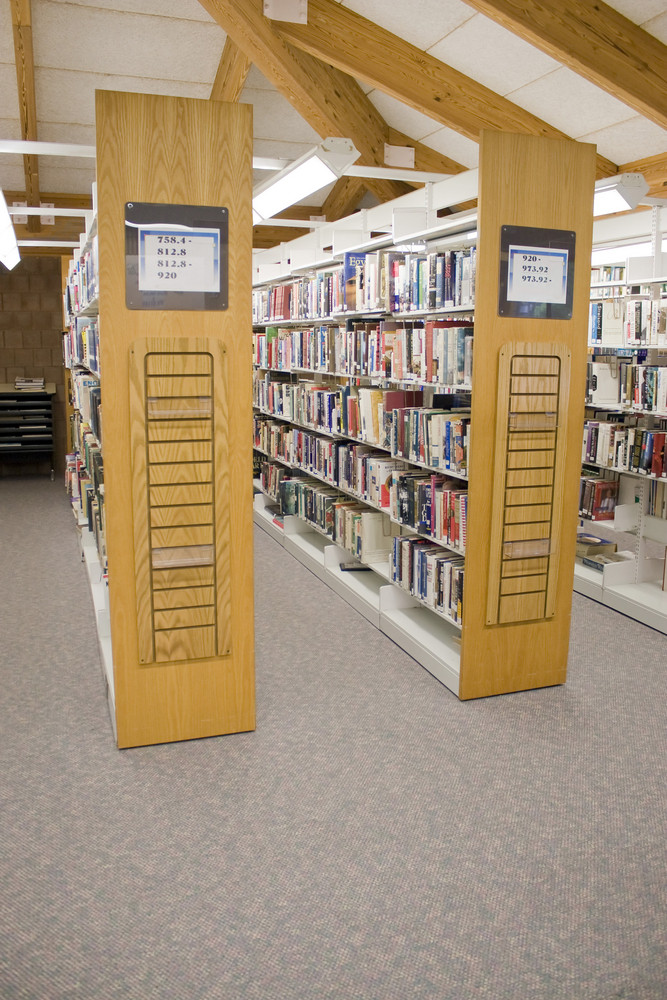 The aisles in a public library with shelves full of books.