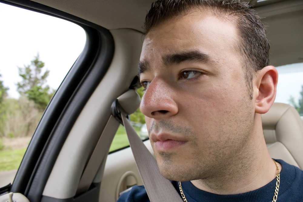 This young man looks bored and stares out the window while riding as a passenger on a long road trip.