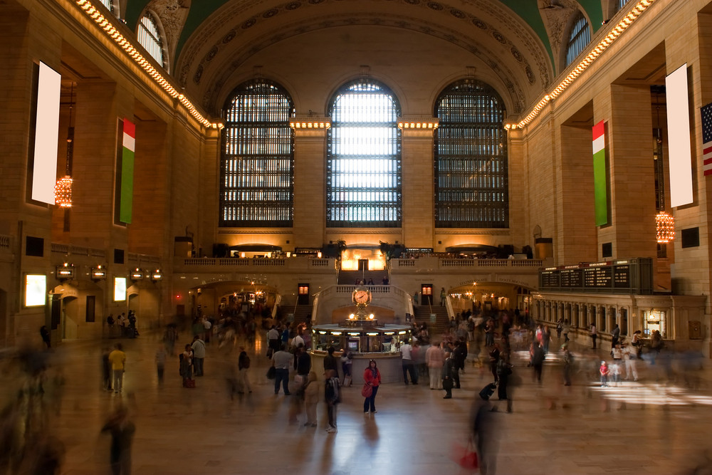Time lapse photo of blurred people walking through Grand Central Terminal train station in New York City with one recognizable woman standing alone in the center.