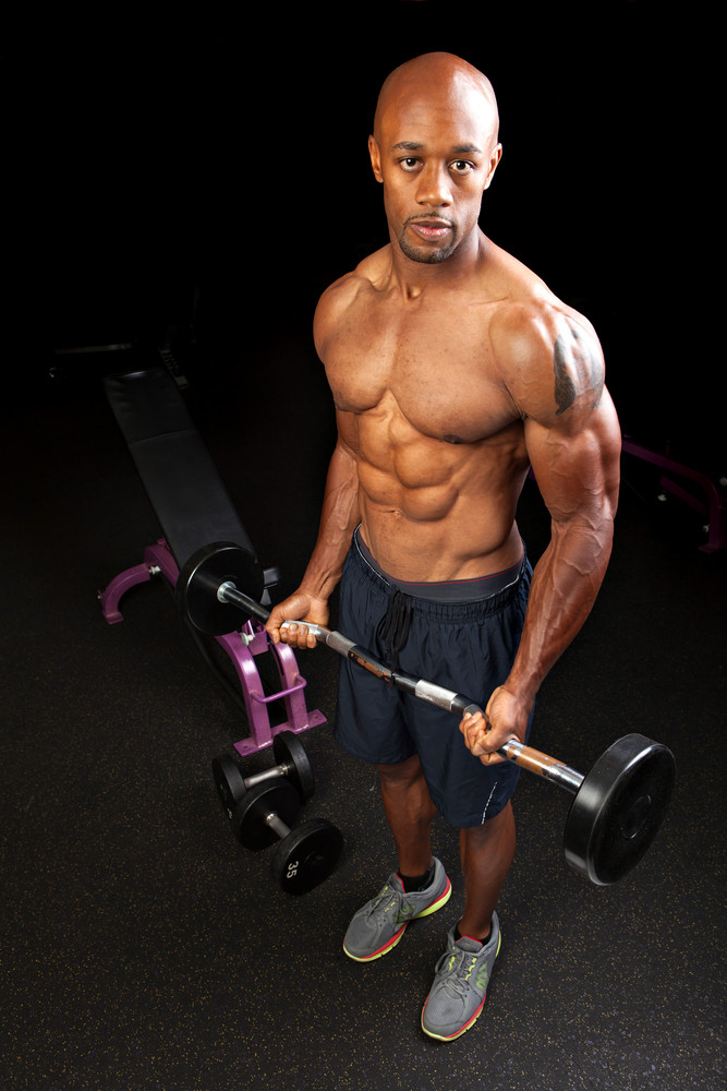 Toned and ripped lean muscle fitness man lifting weights on a curling bar.
