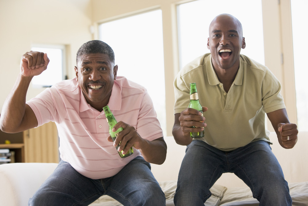 Two Men In Living Room With Beer Bottles Cheering And