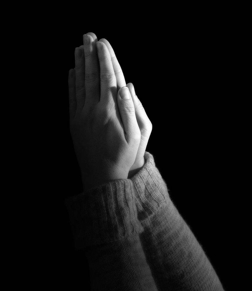 Woman\'s hands held up in prayer on black background.