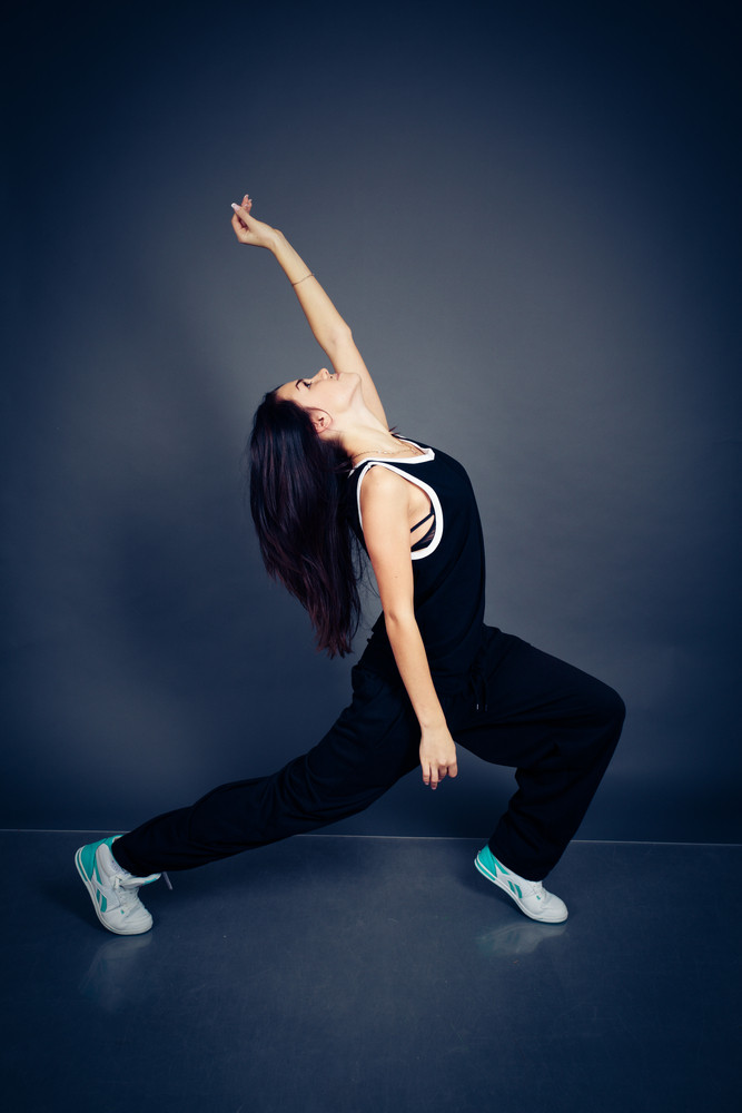 Young beautiful dancing woman in black hip-hop suit on dark background
