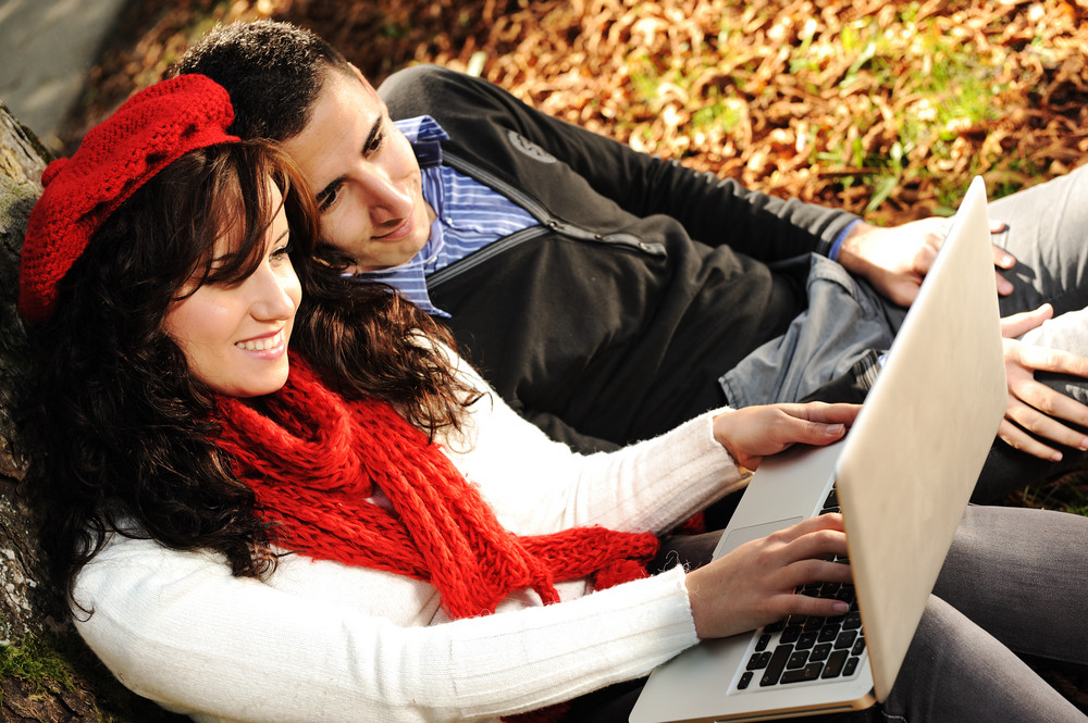 Young couple, male and female sitting in park and studing and workind together with notebook , fall period