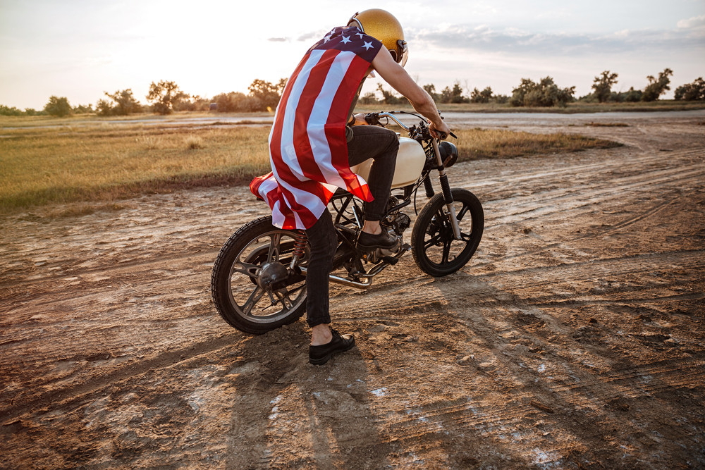 Man in golden helmet and american flag cape starts his motorcycle