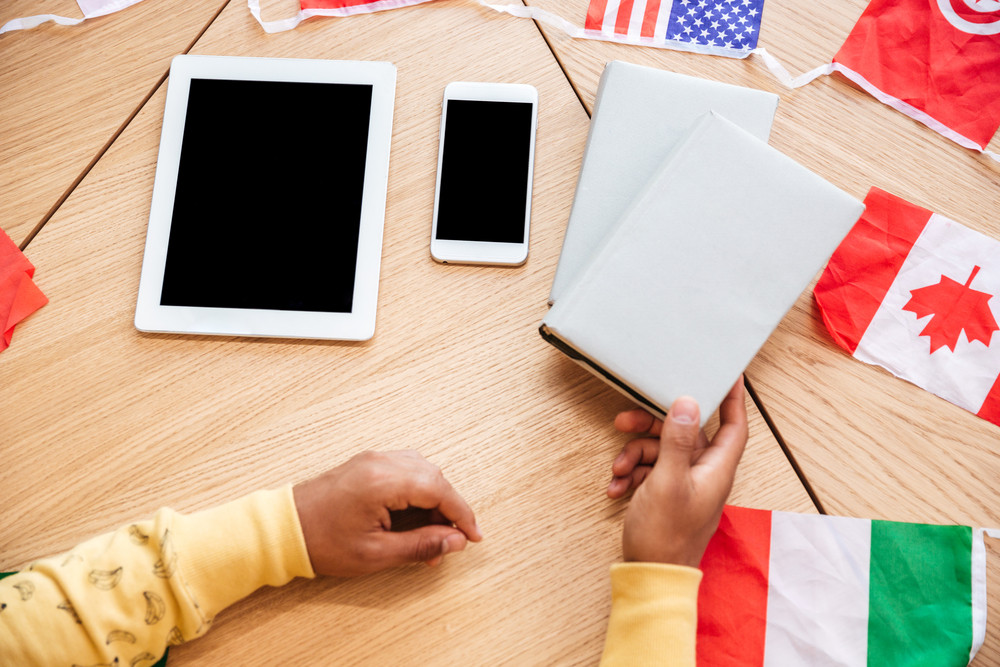 Top view of man at the table with books, blank screen cell phone, tablet and flags of countries