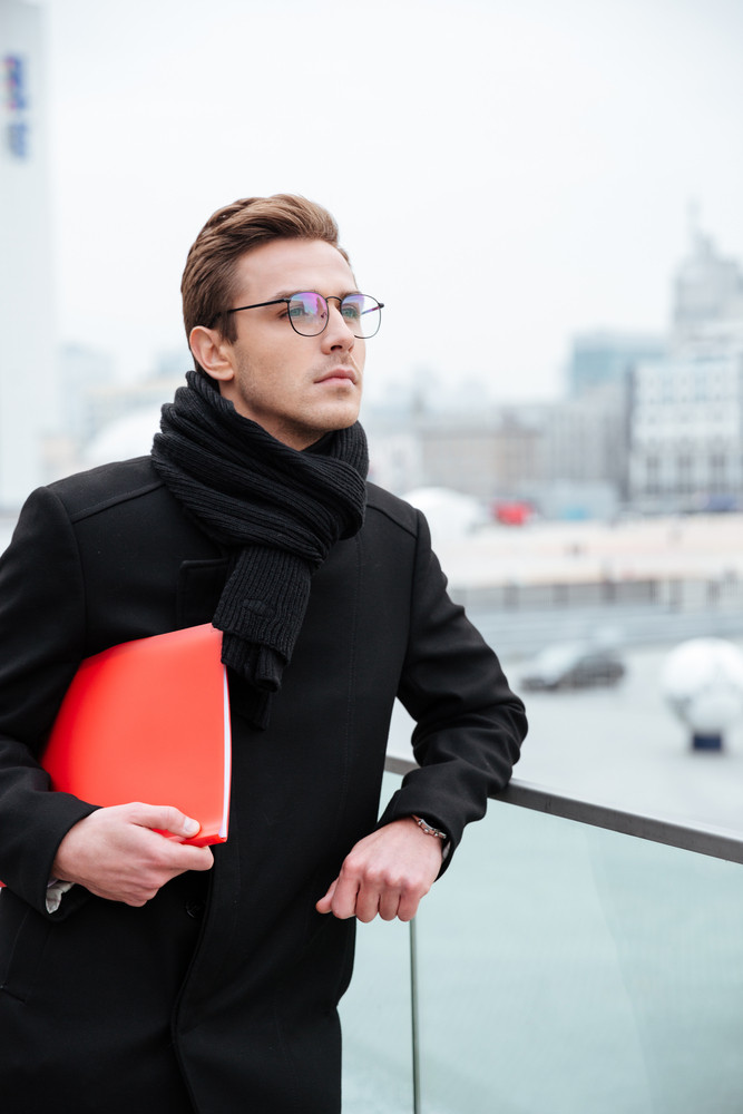 Vertical image of business man in glasses and warm clothes with folder outdoors