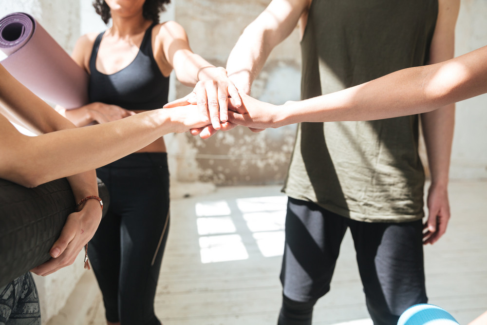 Cropped image of group of healthy pretty people making team gesture while doing yoga in gym