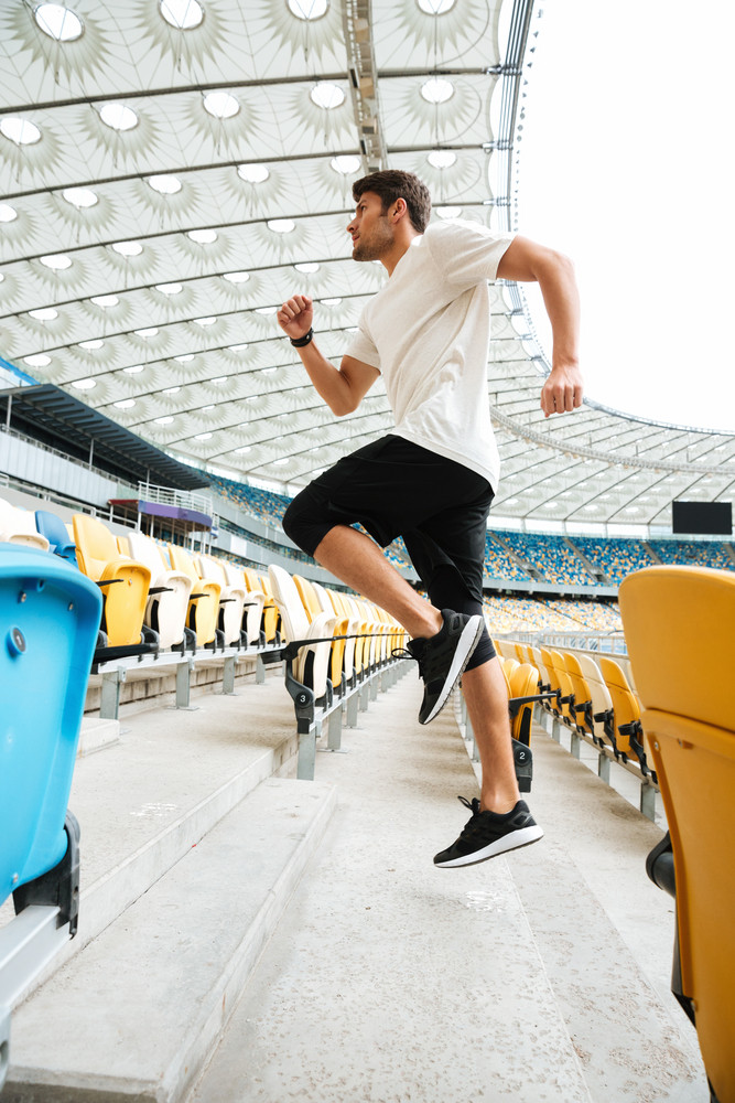 Side view of a sporty athlete man running upstairs at the stadium