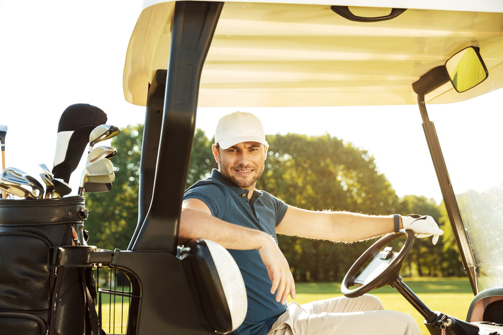Smiling young male golfer sitting in a golf cart and looking at camera