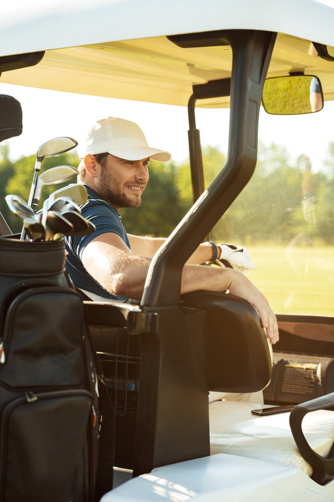 Smiling young male golfer sitting in a golf cart