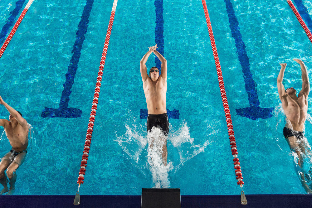 Top view of three male swimmers beginning a back stroke race