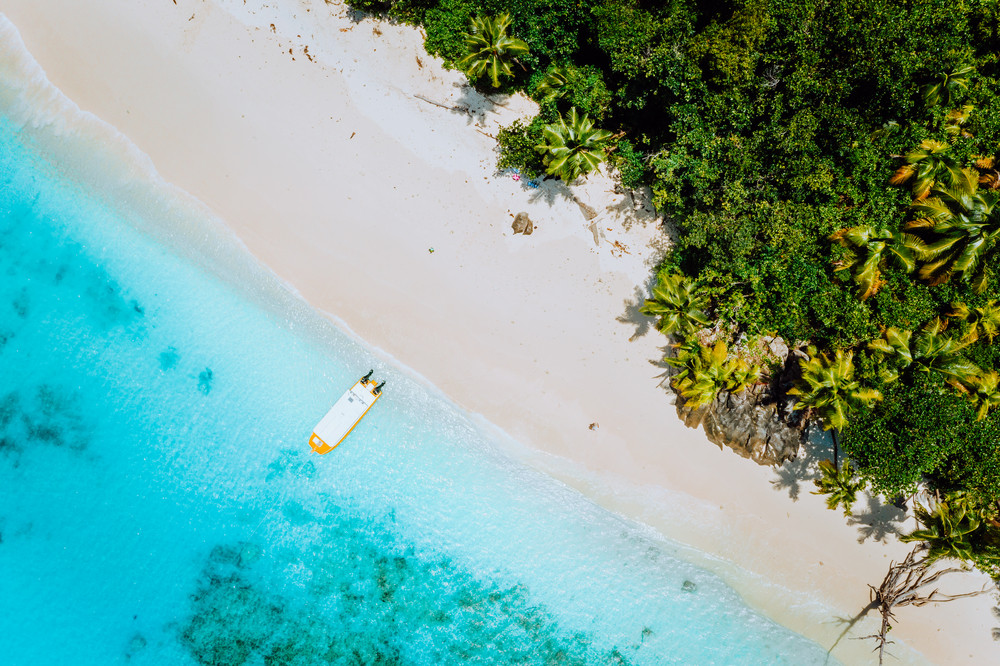 Aerial drone view of paradise beach with coconut trees and lonely tourist boat in turquoise shallow lagoon water