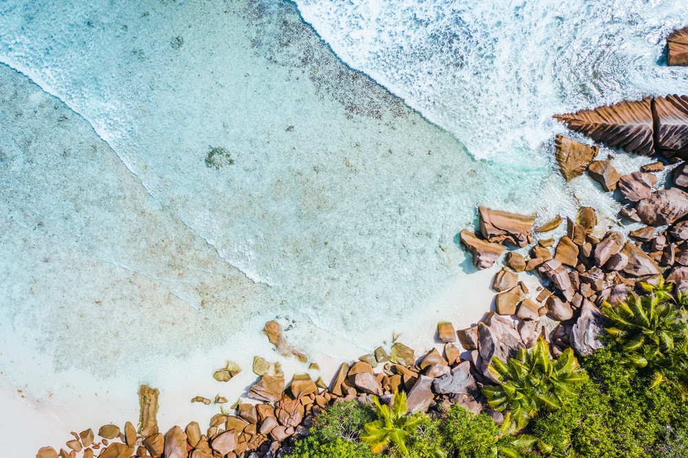 Anse Cocos beach tropical island La Digue Seychelles. Drone aerial view bird-eye perspective at the palm trees and foam ocean waves rolling towards the coast
