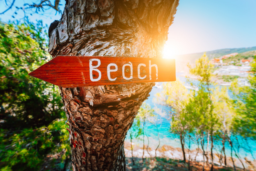 Assos village in morning sun beam light, Kefalonia. Greece. Beach wooden arrow sign on a pine tree showing direction to small hidden beach