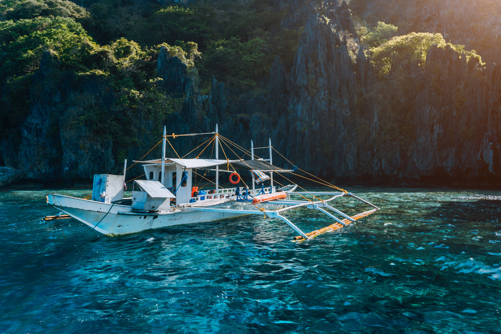 Banca local boat on turquoise water against huge limestone cliffs. Island hopping tour trip. Exploring Philippines summer vacation journey holidays. Marine National Park, Palawan
