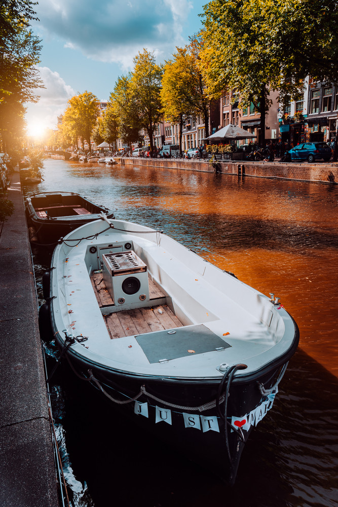 Channel in Amsterdam at autumn sunset. Boat in front of tree-lined canal, white clouds in the sky. Netherlands houses landmark landscape. Romantic City trip concept