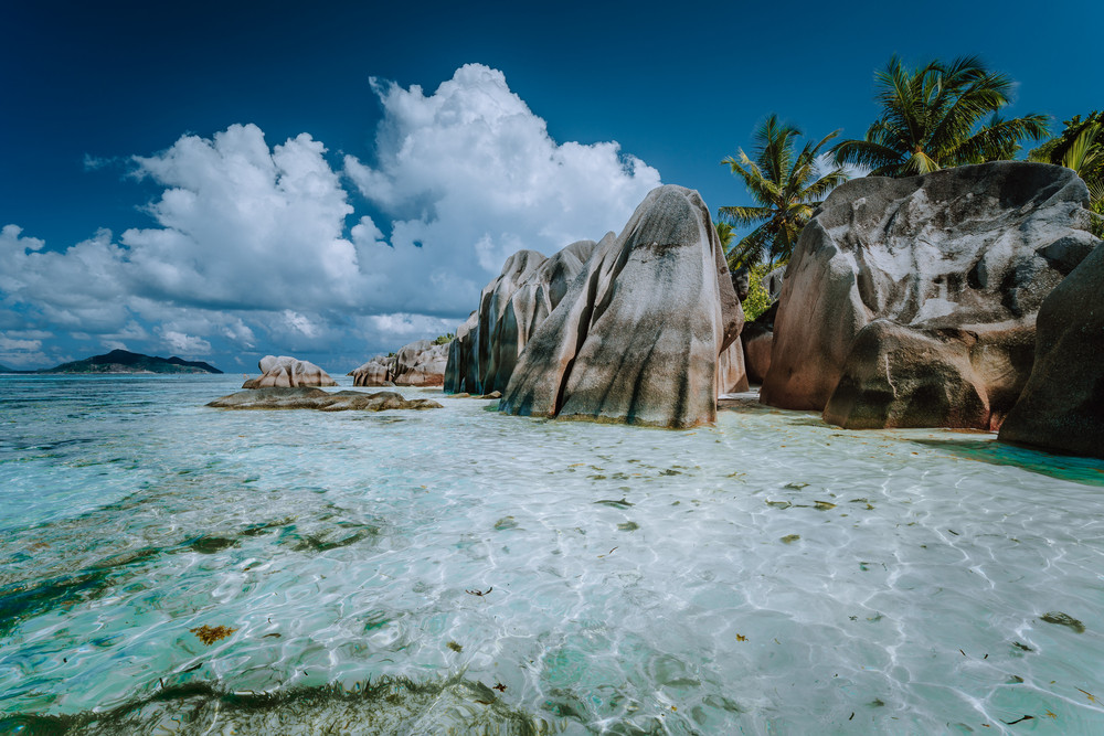 Granite boulders in shallow ocean water and white cloudscape on amazing Anse Source D'Argent tropical beach, La Digue Seychelles. Luxury exotic travel concept