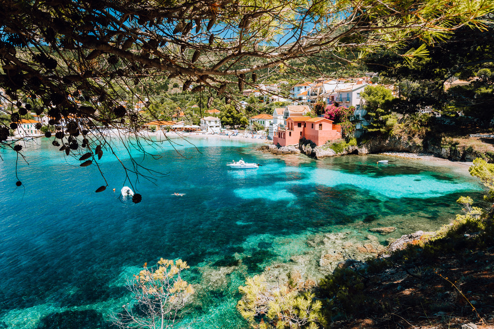 Lovely bay of assos village, Kefalonia, Greece. View on tourquise transparent water framed between green pine grove branches. Deep dark pattern on lagoon bottom