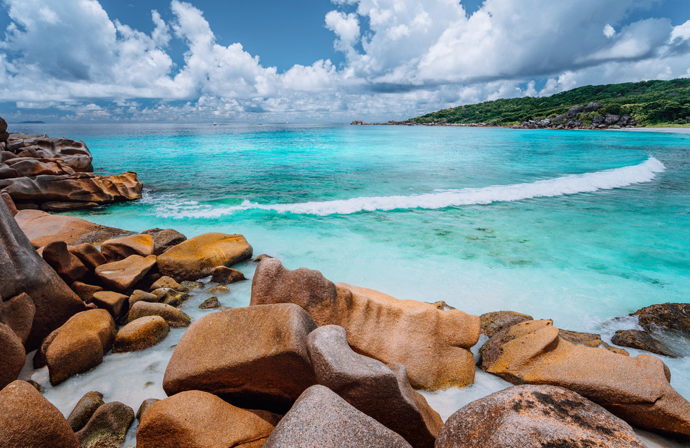Rolling wave and stunning granite formations on the beautiful tropical island with white clouds of La Digue, Seychelles