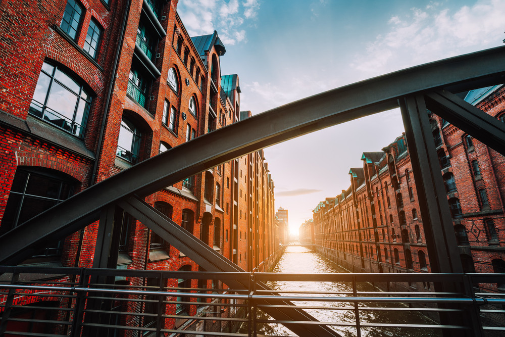 The red brick warehouse - Speicherstadt district in Hamburg Germany, framed by steel bridge arch beams with canal perspective filled by warm sunset light