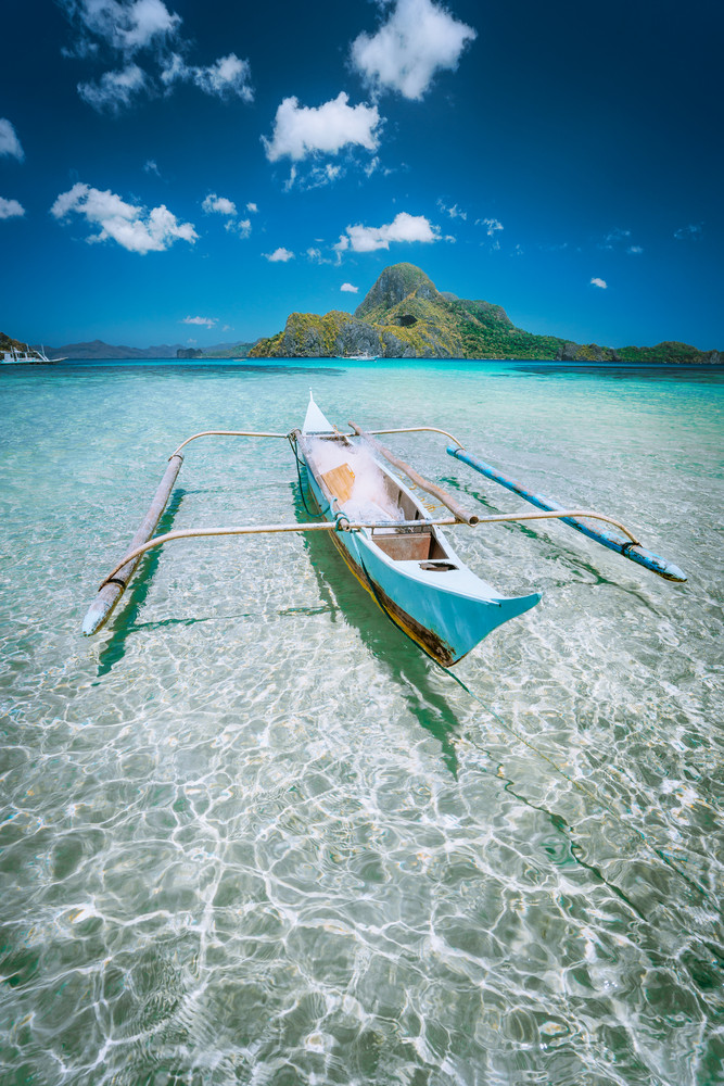 Traditional filippino fisher banca boat in blue lagoon at El Nido bay with Cadlao Island on Background. Palawan Island, Philippines
