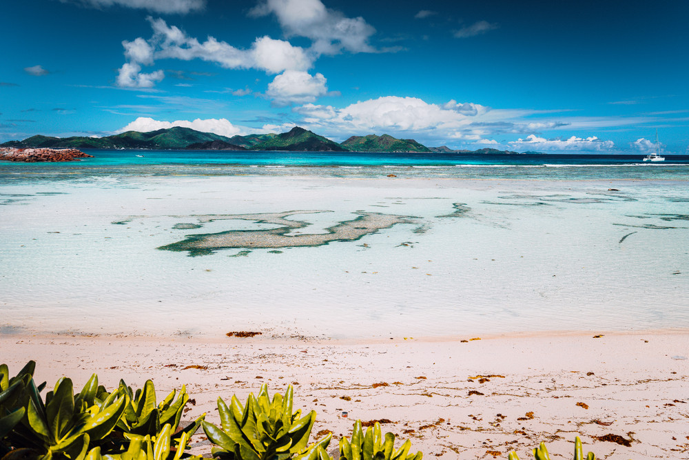 Tropical famous Anse Source d\'Argent beach on sunny day on island La Digue in Seychelles. Praslin Island in Background. Exotic paradise travel scenery concept