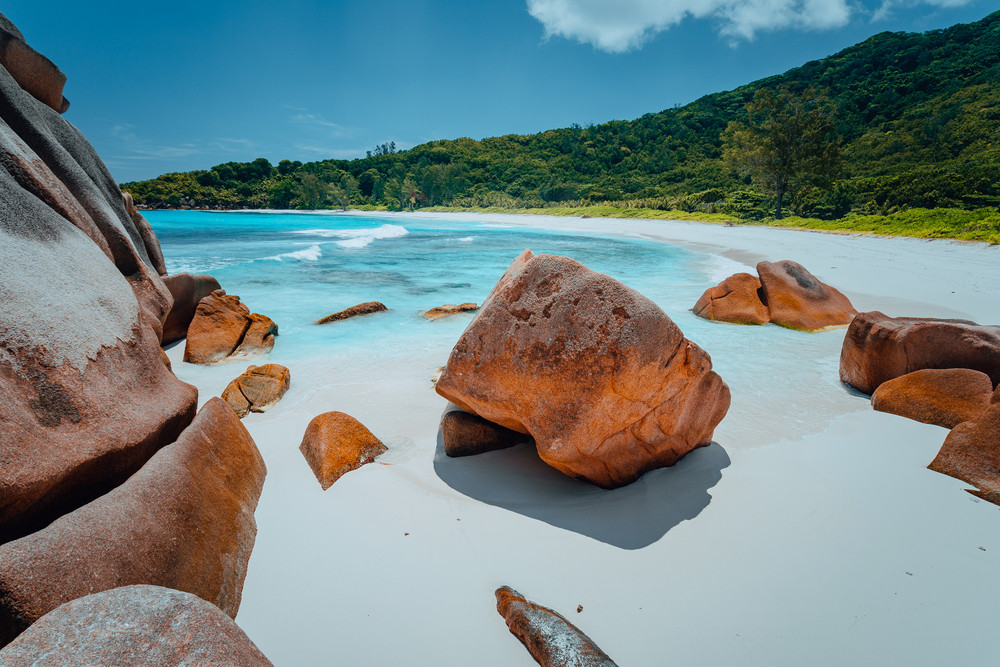 Tropical lagoon with granite boulders in the turquoise water and a pristine white sand at Anse Cocos, La Digue island, Seychelles