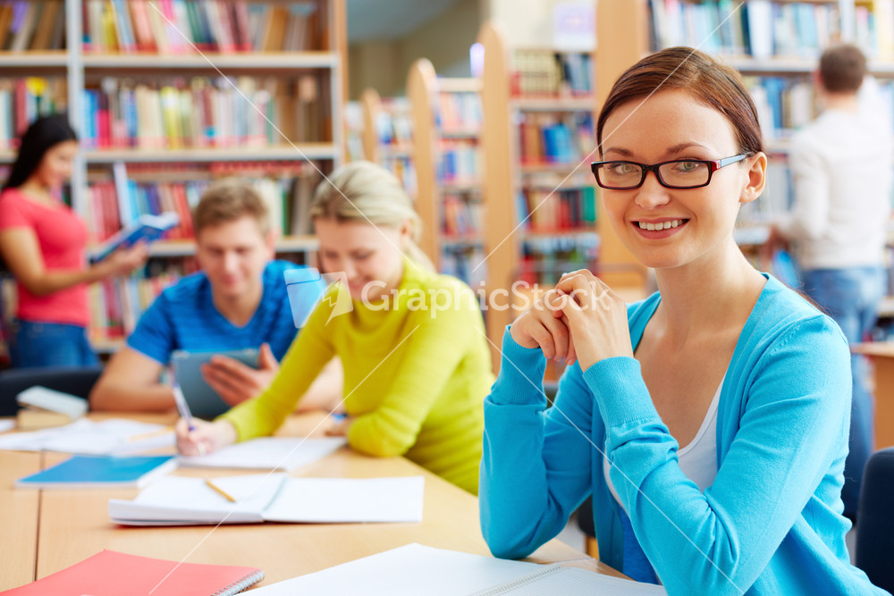 Portrait Of Pretty Girl Sitting In College Library With Her Group Mates On Background