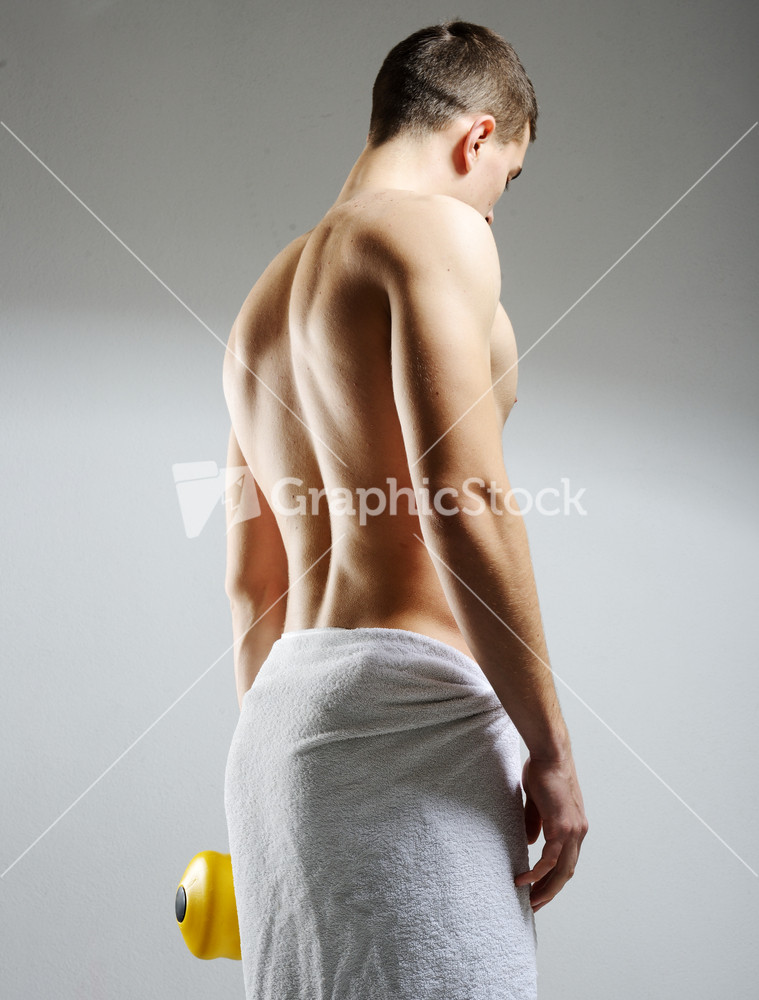 Rear view of a young male bodybuilder doing heavy weight exercise with dumbbells against dark background