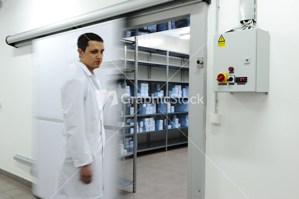 Young worker opening door of industrial refrigerator