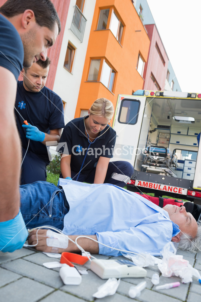 Emergency team examining injured senior patient lying on street